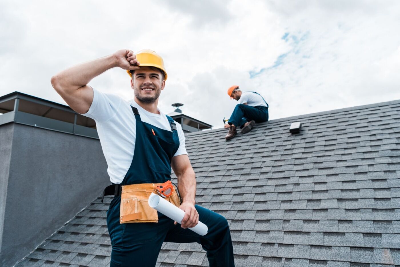 selective focus of happy repairman holding rolled paper while coworker repairing roof